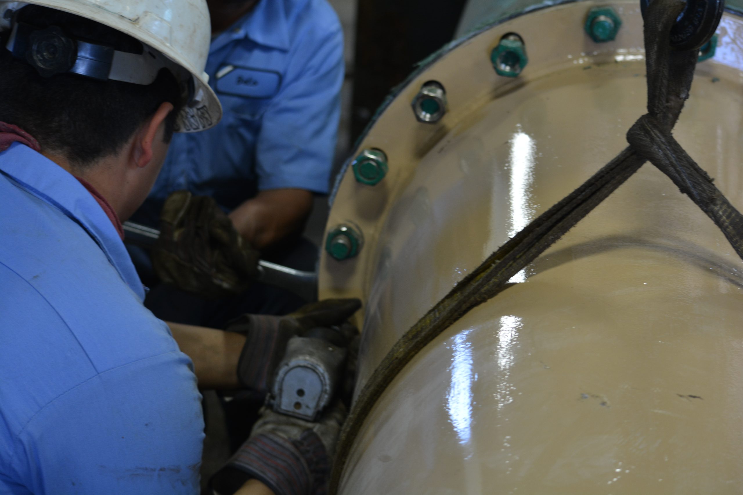Technicians in hard hats working on a large bolted pump column flange with a rigging strap.