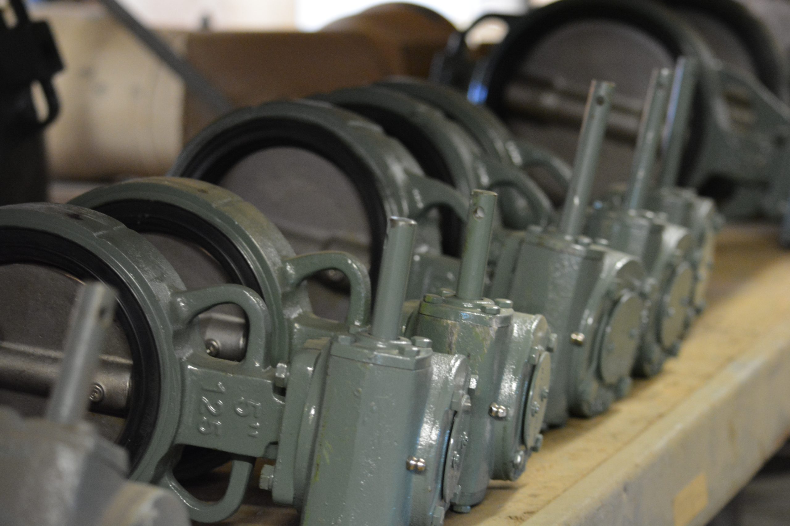 Row of gray butterfly valves with gear actuators lined up on a shop shelf.